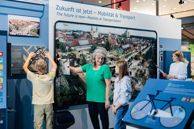 Familie steht vor dem Zukunftsbild im Themenbereich Mobilit&auml;t.